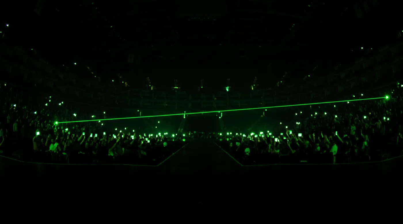 A dark arena crowd watching from the shadows with glowing phone screens held up
